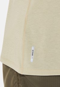 Hellbeiges T-Shirt mit weicher Textur und flachen Nähten, mit einem am Rand aufgenähten ACTIBREEZE-Label.