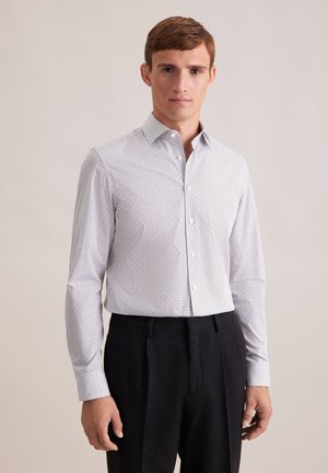 Witte blouse met kleine zwarte stippen, lange mouwen, klassieke kraag, gecombineerd met donkere op maat gemaakte broek.