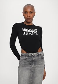 Top preto de manga longa com texturas em nervuras apresentando o texto "MO5CH1NO JEANS", combinado com uma saia de ganga cinza de cintura alta. Textura suave e design ajustado.