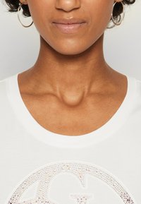 Camiseta blanca con cuello redondo que presenta un gráfico brillante en rhinestones multicolores y una suave textura de algodón.