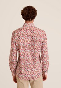 Langarmshirt met een rood, roze en groen bladenpatroon op een witte achtergrond. Standaardkraag, knoopmanchetten en een afgeronde zoom.