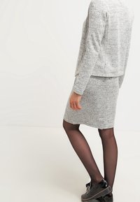 Suéter gris texturizado combinado con una falda lápiz gris, ambos con un patrón sutil. Zapatos negros con un acabado suave y suelas ligeras.