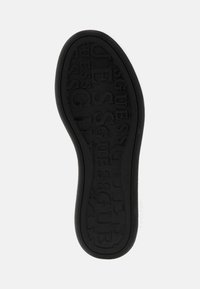 Black rubber shoe sole with textured "GUESS" logo in various orientations. Smooth edges and slightly raised border. Flat profile.