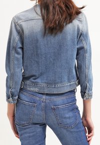 Ljusblå denimjacka med en urtvättad finish, figursydd design, knappradier och en kortad nederkant. Matchas med matchande denimjeans.