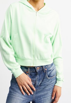 Haut à capuche zippé vert menthe avec une capuche, des poignets et un ourlet côtelés ; comprend des poches latérales et un petit logo sur la poitrine ; associé à un jean bleu.