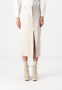 Beige midi rok met een voorknoping, nauwsluitende pasvorm en soepel materiaal. Gecombineerd met beige plateau-schoenen en bijpassende sokken.