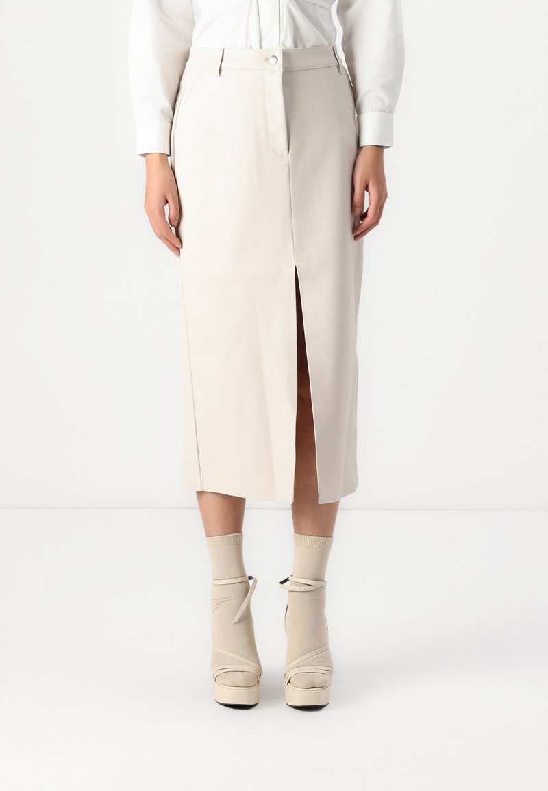 Beige midi rok met een voorknoping, nauwsluitende pasvorm en soepel materiaal. Gecombineerd met beige plateau-schoenen en bijpassende sokken.