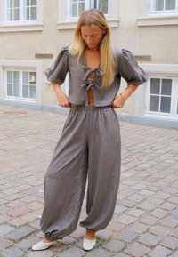 Femme ajustant un pantalon ample à taille haute à carreaux et un haut à manches courtes assorti avec des liens devant, debout dans une rue pavée.