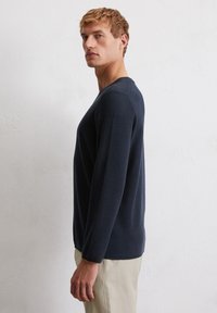 Granatowy sweter z długim rękawem wykonany z dzianiny o teksturowanej strukturze, z okrągłym dekoltem i ściągaczem na dole, w połączeniu z jasnobeżowymi spodniami.