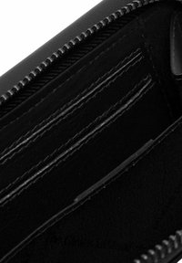 Intérieur de portefeuille noir avec des poches en cuir lisse, plusieurs emplacements pour cartes et un compartiment zippé. Doublure en tissu texturé visible.