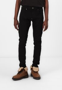 Jean slim noir avec fermeture à bouton et poches avant, associés à des bottes à lacets marron avec un col en fourrure.