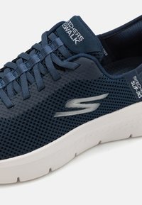 Navy mesh sneaker with a white sole, featuring a textured overlay, smooth laces, and a logo accent on the side and heel.