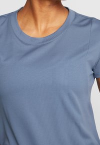 Světle modré tričko s krátkými rukávy a kulatým výstřihem, vyrobené z texturované látky, s jemným mřížkovým vzorem a zesílenými švy.