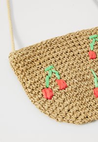 Geflochtene Strohtasche in Halbmondform mit roter Kirschen-Stickerei und grünen Stielen, ausgestattet mit einem Trageriemen aus Naturfaser.