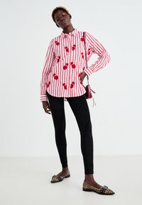 Chemise rayée rouge et blanche avec motifs floraux, leggings noirs et ballerines imprimé léopard. Le mannequin porte un petit sac rouge.