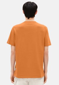 Orange Baumwoll-T-Shirt mit kurzen Ärmeln und Rundhalsausschnitt, ausgestattet mit einem schlichten Design und einem sichtbar an der unteren Seite angebrachten Etikett.
