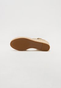 Lysebrunt vævet platform sandal med en tekstureret korksål og gyldent hardware. Har en bred rem og justerbar spænde for tilpasning.