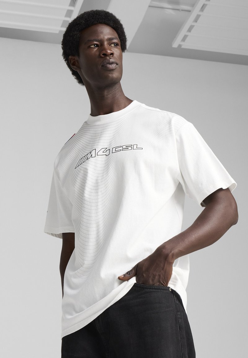 Hvid kortærmet T-shirt lavet af bomuld, med et grafisk "M4CSL" tryk i sort. Glat tekstur med en oversized pasform.