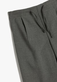 Graue Stoffhosen mit strukturiertem Obermaterial, Falten an der Vorderseite und einem Kordelzugbund. Maßgeschneiderter Schnitt mit lockerem Sitz.