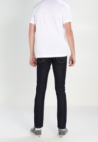 Jean slim bleu foncé associé à un t-shirt blanc uni, présenté de dos, avec des coutures discrètes et une taille standard.