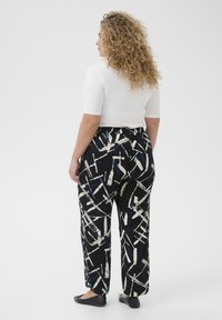 Loose-fitting black and white patterned pants with abstract lines, paired with a fitted white top. Soft texture and straight-leg design.