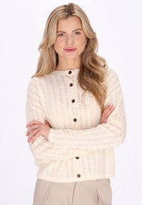 Crèmekleurig vest met een getextureerd breipatroon, een ronde halslijn en bruine knopen. Het heeft lange mouwen en een cropped pasvorm.