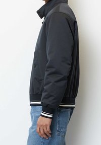 Giubbotto bomber da uomo grigio scuro con colletto alto, tasche frontali e polsini a costine. Presenta dettagli a strisce bianche in vita.