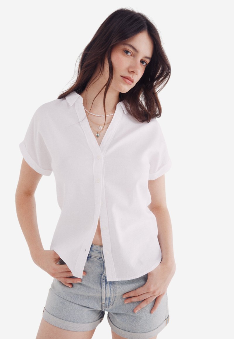 Witte korte mouwen button-up shirt met een kraag, textuurstof en een relaxte pasvorm, gecombineerd met lichte denim shorts.