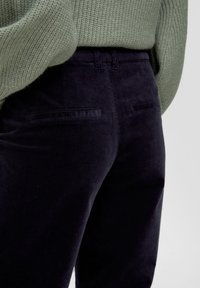 Marineblauwe corduroy broek met een gestructureerde afwerking en twee achterzakken, gecombineerd met een lichtgroene gebreide trui.