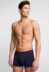 Navy blue boxer briefs with a red-bordered elastic waistband. Made from a soft fabric, featuring a snug fit and seam detailing.