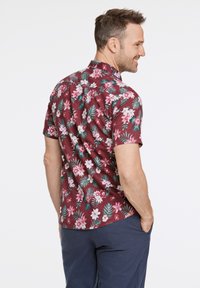 Camicia a maniche corte di colore bordeaux con un motivo floreale che presenta fiori bianchi e rosa, foglie verdi e un design di colletto classico.