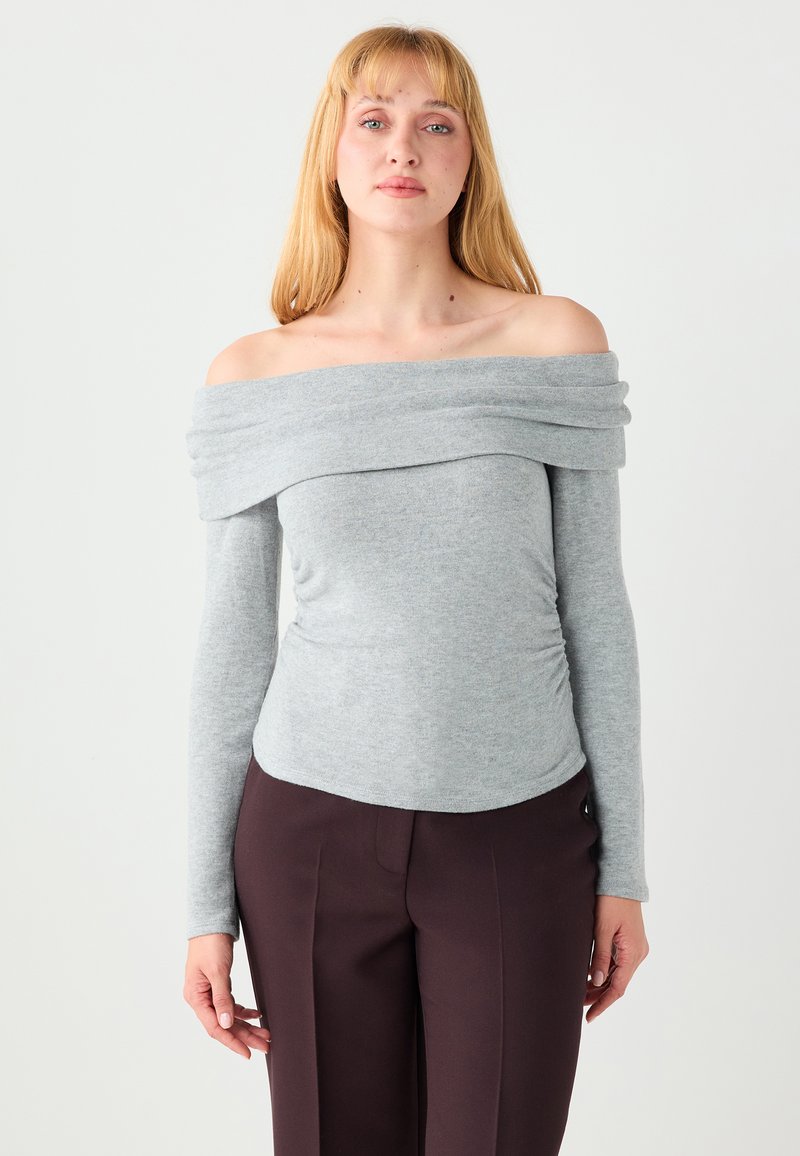 Haut gris épaules dénudées avec manches longues, texture douce, côtés froncés et encolure drapée, associé à un pantalon foncé.