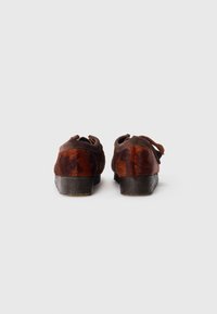 Brown leather shoes with a textured finish. Rounded shape, low heel, and ribbon accents. Fur-like material on sides with varied coloration.