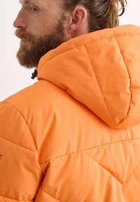 Chaqueta acolchada naranja con diseño acolchado, capucha y textura suave. Incluye herrajes ajustables para un ajuste personalizado.