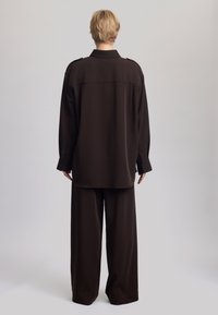 Barna túlságosan nagy ing és hozzá illő széles szárú nadrág puha anyagból, klasszikus gallérral és gombos mandzsettával.