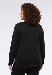 Langärmliges schwarzes Shirt aus weichem Stoff, mit abgerundetem Saum und seitlichen Schlitzen für optimale Bewegungsfreiheit. Glatte Textur, minimalistisches Design.