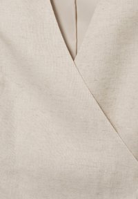 Gros plan sur un tissu en lin beige avec un pli chevauchant en forme de V, montrant les détails de la texture et des coutures.
