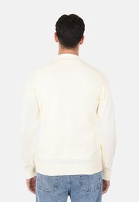 Maglione a maglia giallo chiaro con maniche lunghe, polsini a coste e scollo tondo. Texture liscia, dettagli minimi all'orlo.