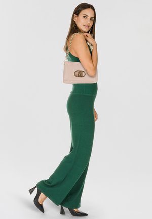 Tuta verde senza maniche in tessuto elasticizzato, abbinata a una borsa rosa chiaro con tracolla a catena e chiusura decorativa. Scarpe con tacchi alti nere.