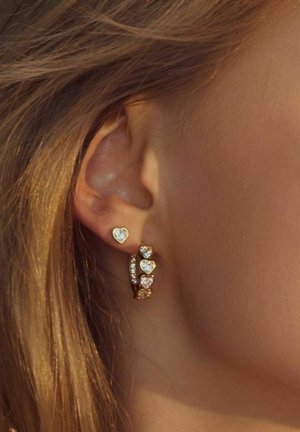 Guldtonede øreringe med små hjerte-stud og et hoop-design udsmykket med flere hjerteformede sten, der fremviser en glitrende finish.