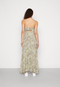 Maxikleid aus leicht grünem Stoff mit kleinen Blumenmustern, verstellbaren Spaghettiträgern, einer Schleifendetail hinten und einem Ausschnitt in Tropfenform.