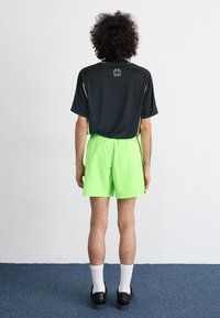 Tricou sportiv negru cu accente verzi, purtat împreună cu şorturi verzi strălucitoare. Are o croială lejeră și o lungime până la genunchi. Pantofi negri și șosete albe.