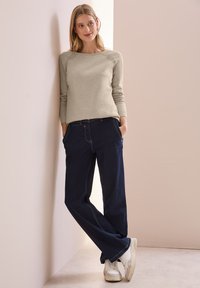 Beige langärmliger Pullover mit Raglanärmeln, kombiniert mit dunkelblauen weiten Jeans, getragen mit weißen Sneakers. Einfaches, minimalistisches Design.