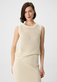 Cream mesh sleeveless top with a ribbed neck and hem, featuring an open knit pattern and relaxed fit. Paired with a matching skirt.