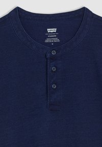 T-shirt henley bleu marine en tissu doux, avec un col rond, trois boutons et une étiquette avec des instructions d'entretien.