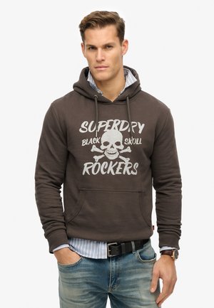 Sudadera marrón oscuro con un bolsillo frontal, que presenta un gráfico de una calavera y huesos cruzados en blanco. El tejido suave acentúa un diseño casual.