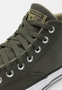 Zelené plátěné tenisky vysokého střihu s kovovými očky, texturovanými tkaničkami a kontrastní bílou gumovou podrážkou. Označení značky na jazyku.