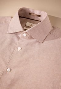 Light pink button-up shirt with a textured fabric, stiff collar, and three white buttons on the front. Tags visible inside the collar.