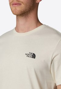 Cremefarvet t-shirt lavet af blødt stof. Har et lille sort trykt logo på venstre bryst. Rund halsudskæring og korte ærmer.