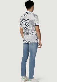 Korte mouwen shirt met een witte achtergrond en verschillende blauwe geometrische patronen, gecombineerd met lichtblauwe jeans en witte sneakers.